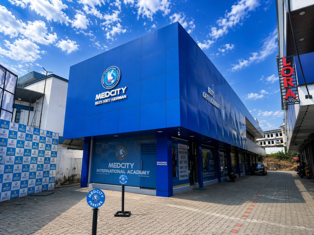 Exterior view of Medcity International Academy featuring its blue branded building and signage for IELTS, OET, German language, PTE and NCLEX-RN training.