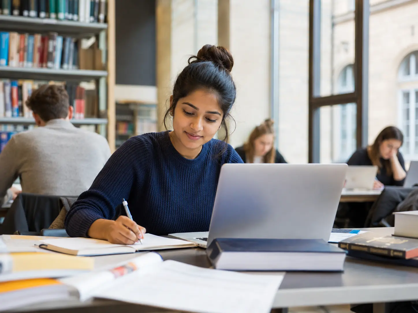 Best German Language Course in Kannur for A1 to B2 Classes 5 Student studying with a laptop and writing notes in a modern library while preparing for the IELTS exam at Medcity International Academy for study abroad and international university admissions.